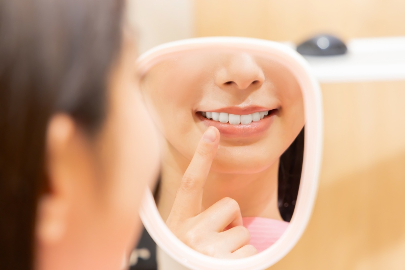 A smiling person checking teeth in a mirror after cosmetic dentistry in Mokena, IL
